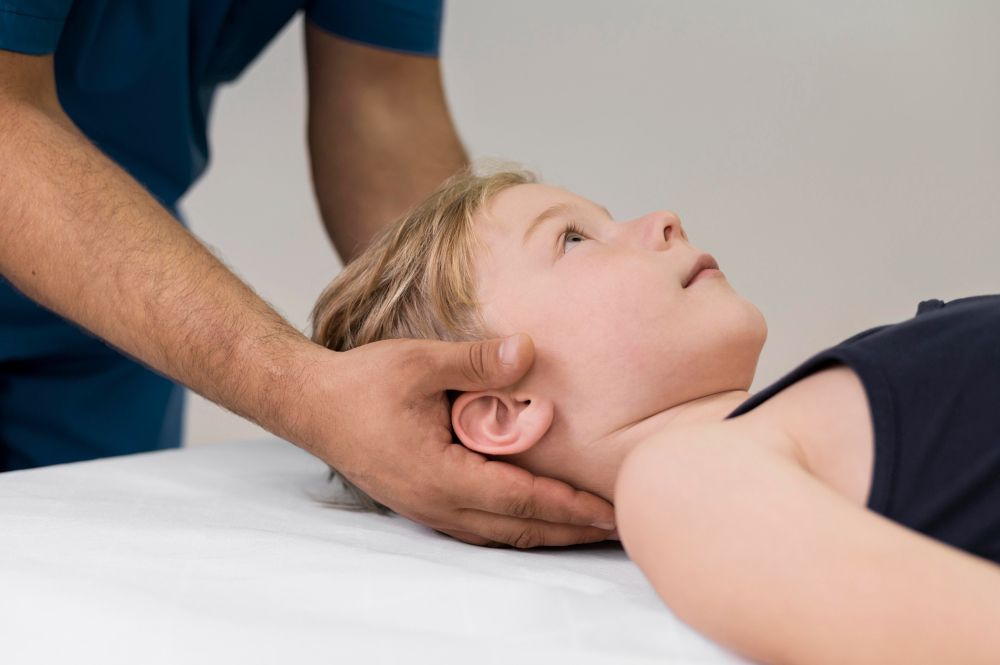 A person's hands gently supporting a child's head and neck. The child is lying down, looking up.