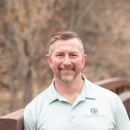 Man in a light green polo shirt smiles; outdoor setting; logo on shirt.