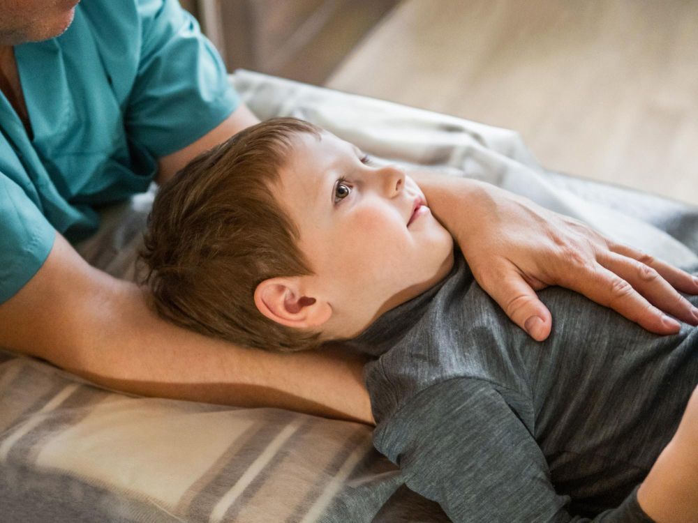 Person in teal shirt examines a young child lying down, hands on the child's body.