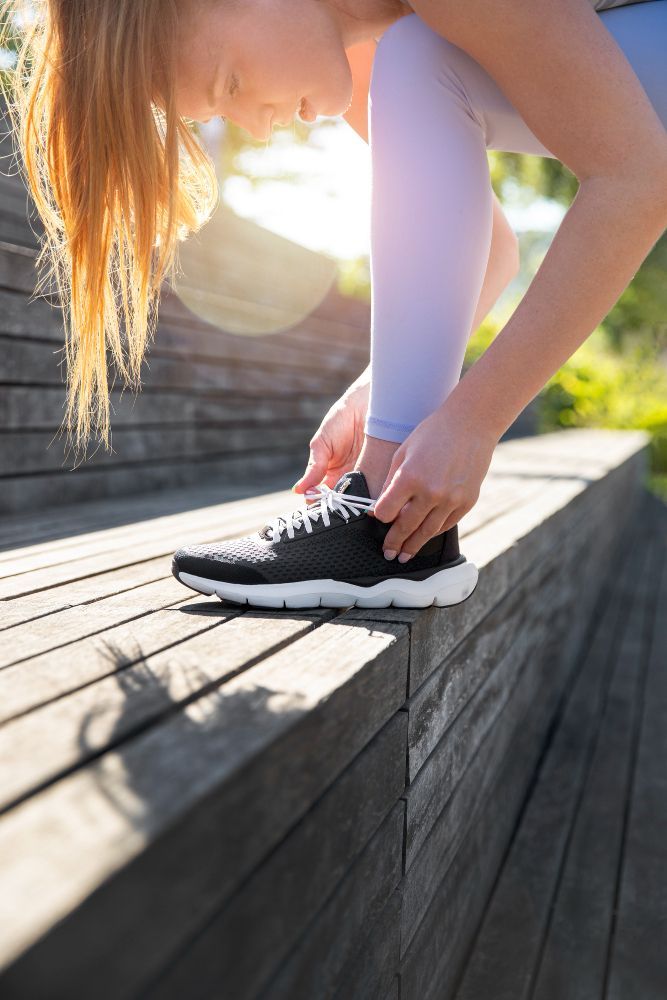 Woman tying running shoe on wooden steps, outdoors.