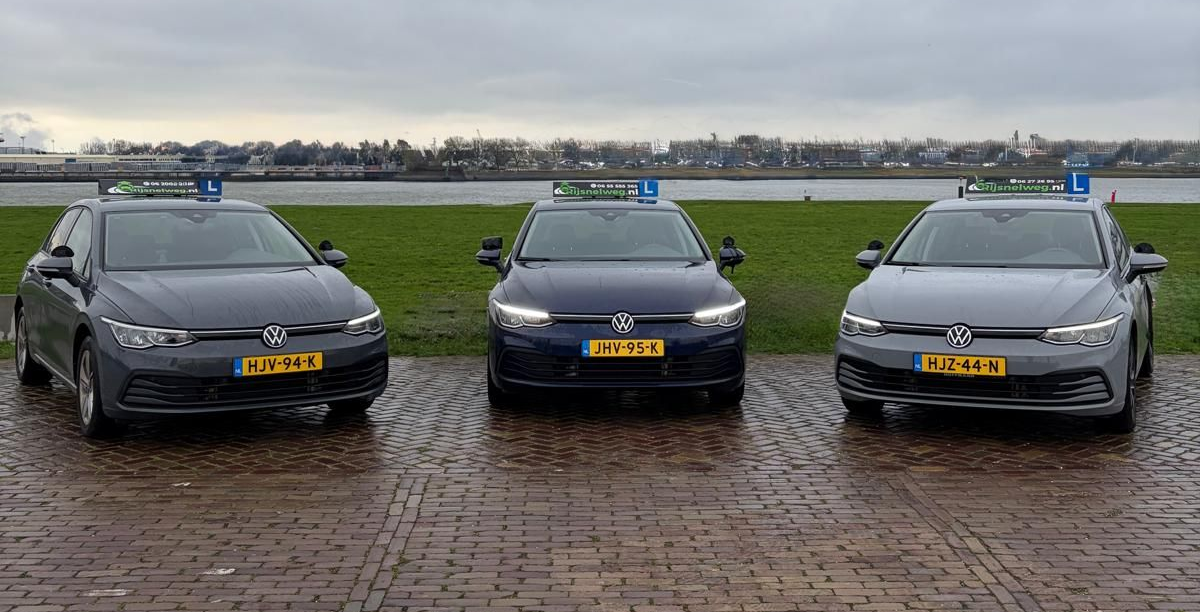 Een persoon die met een instructeur in een auto rijdt. De bestuurder houdt zijn rijbewijs naast een bord.