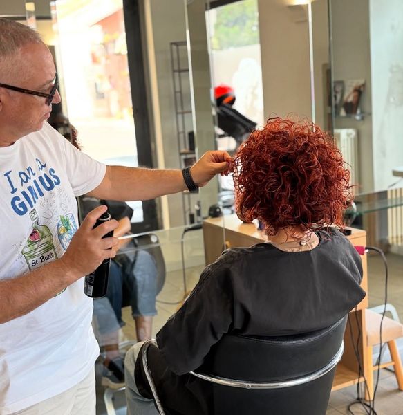 Un parrucchiere spruzza il prodotto sui capelli rossi e ricci di una cliente in un salone di bellezza.