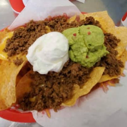 Nachos with meat, guacamole, sour cream, and cheese in a red basket.
