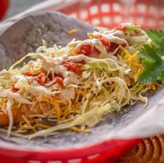 Taco in a basket, with shredded lettuce, cheese, sauce, and cream.