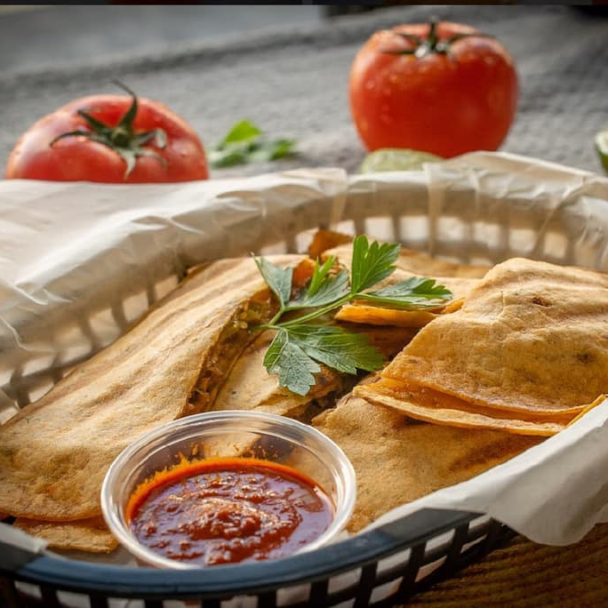 Quesadillas with salsa in a basket, tomato in the background.