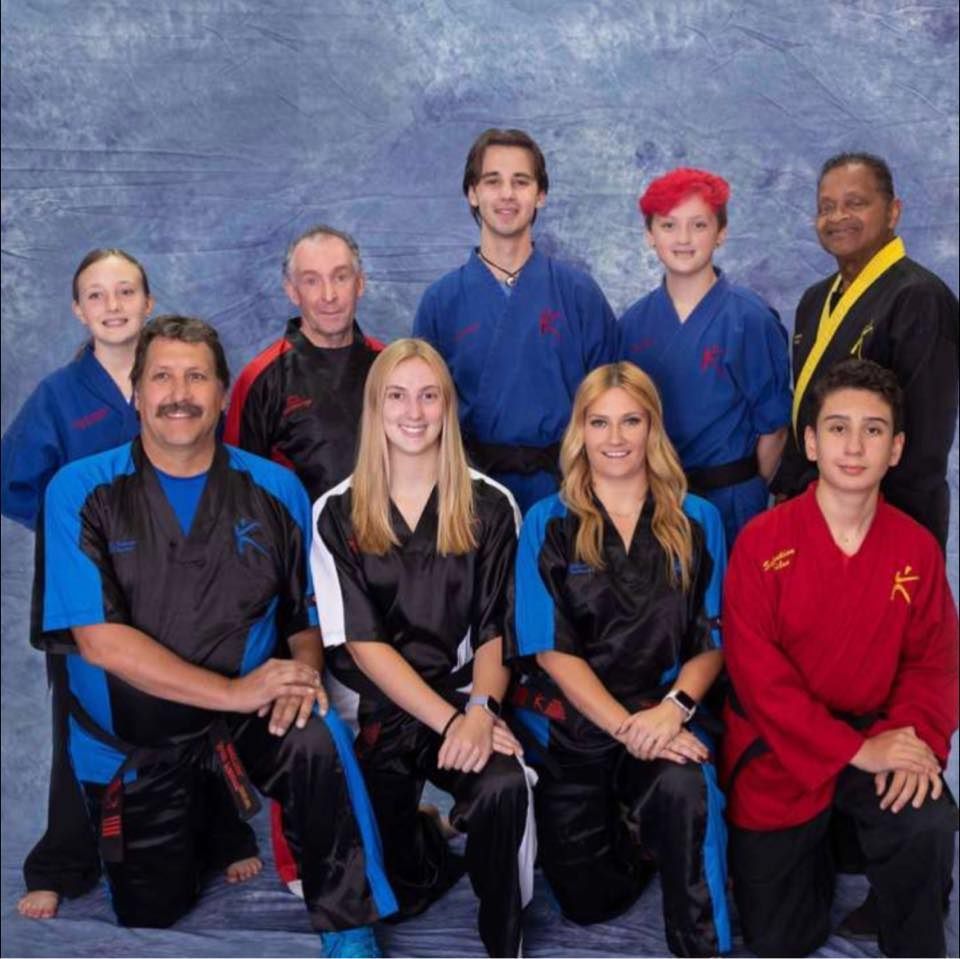 A group of people posing for a picture with one man wearing a blue shirt with the letter k on it