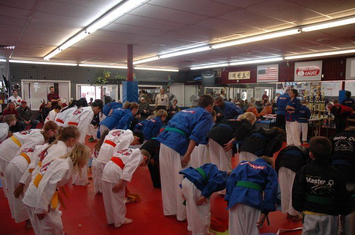 A group of people in karate uniforms are kneeling down in a gym.