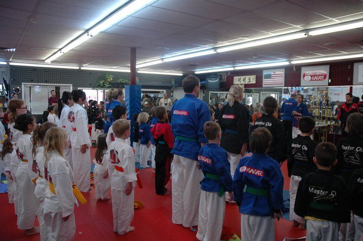 A group of children in karate uniforms are standing in a gym.