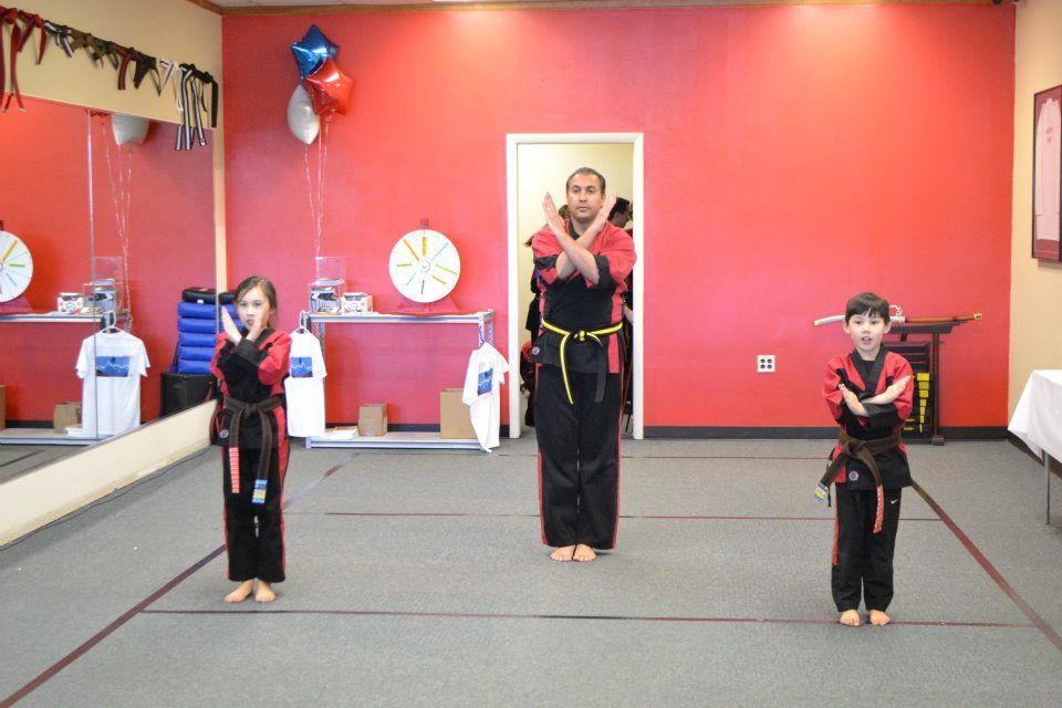 A man and two children are practicing martial arts in a gym