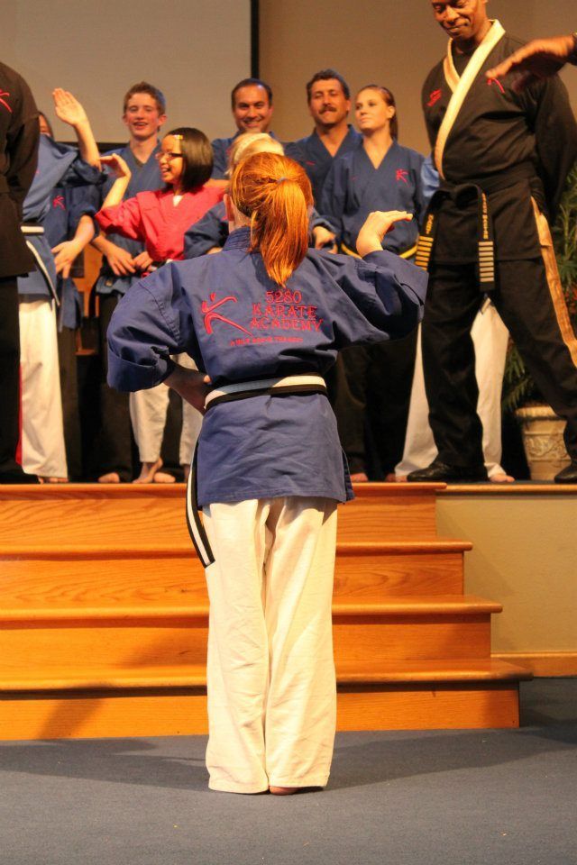 A girl in a blue karate uniform stands in front of a group of people