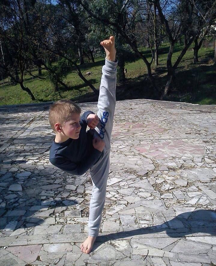A young boy is doing a split on a stone walkway