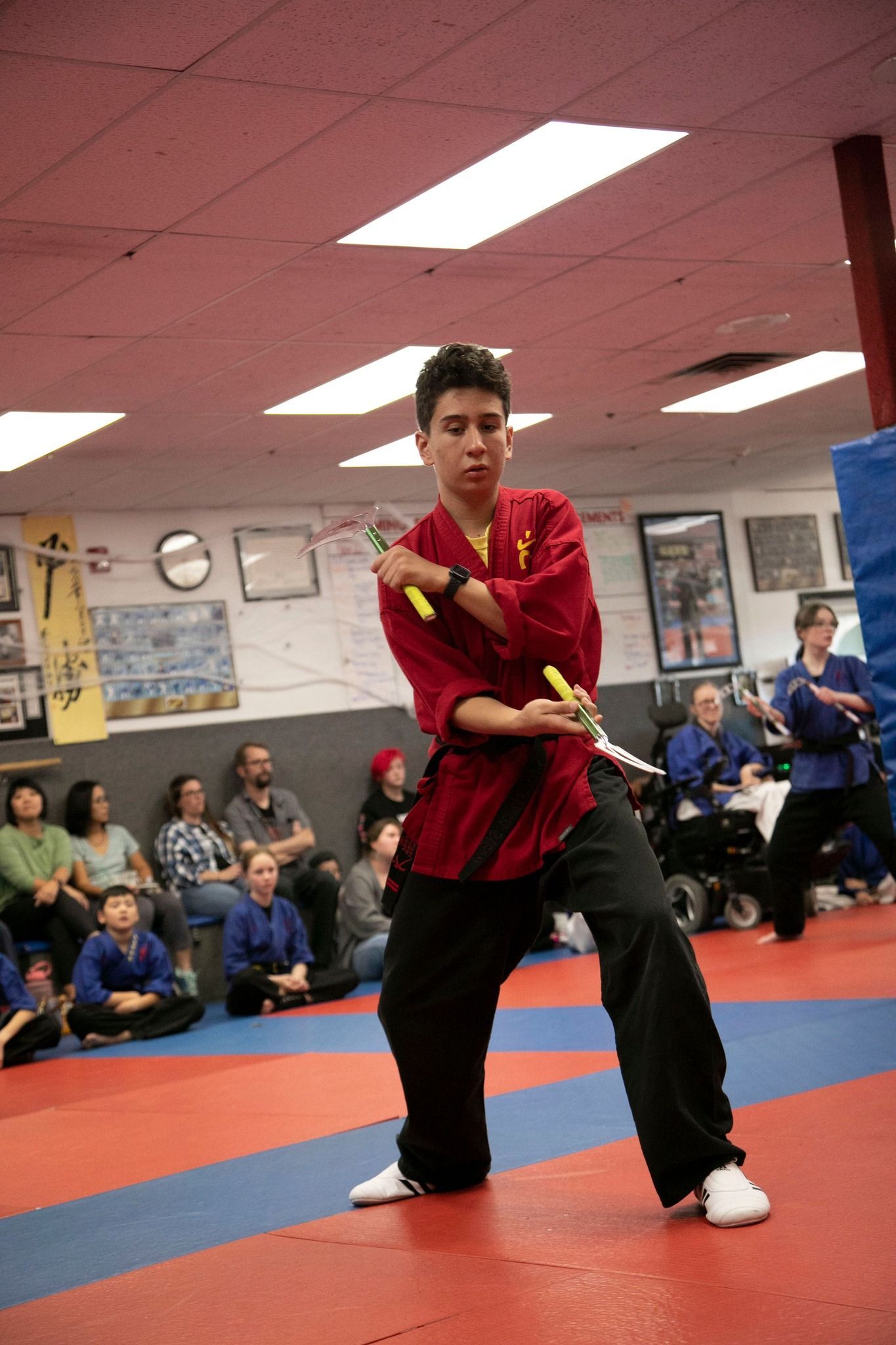A young man is practicing martial arts in a gym while people watch.