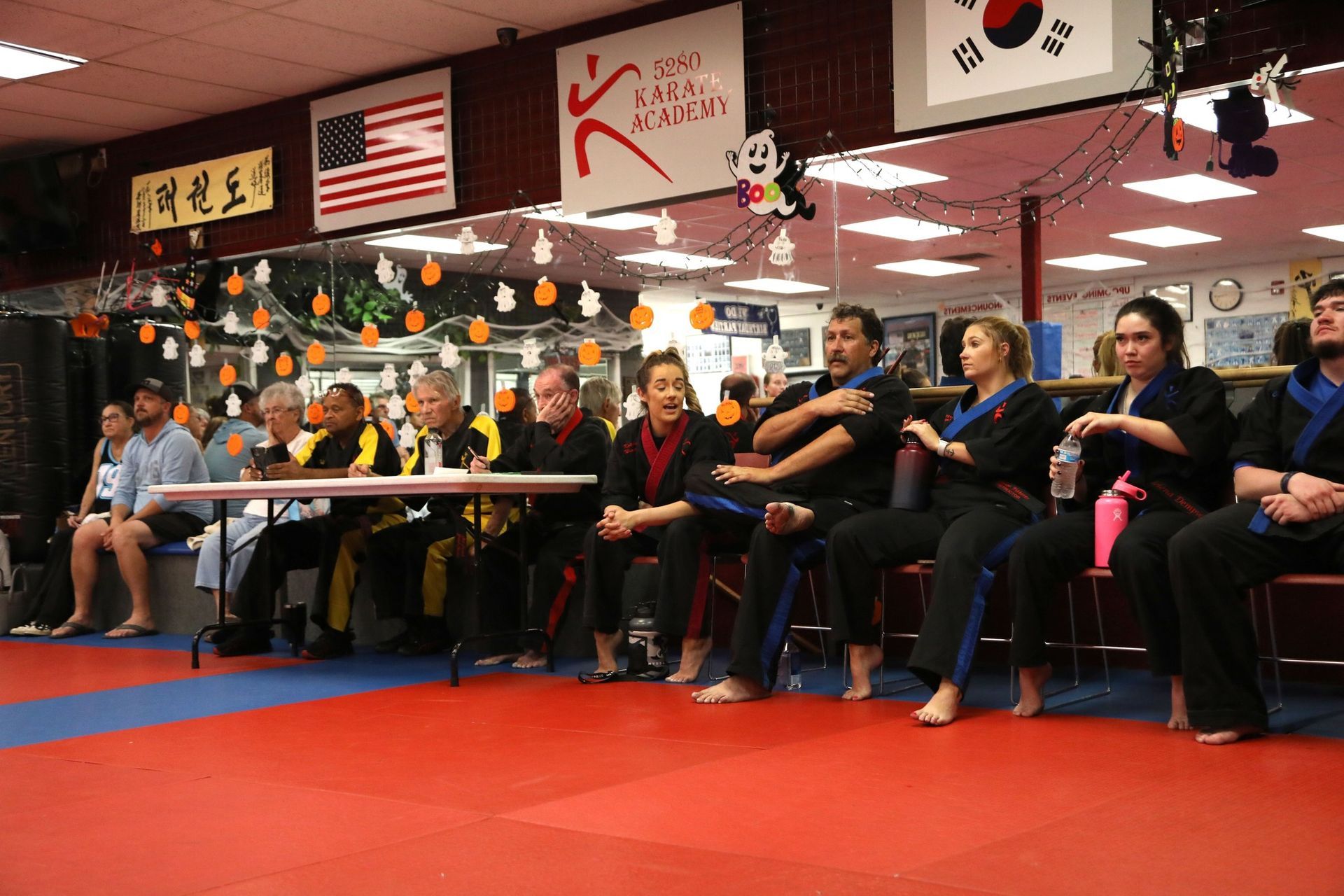 A group of people are sitting at a table in a martial arts gym.