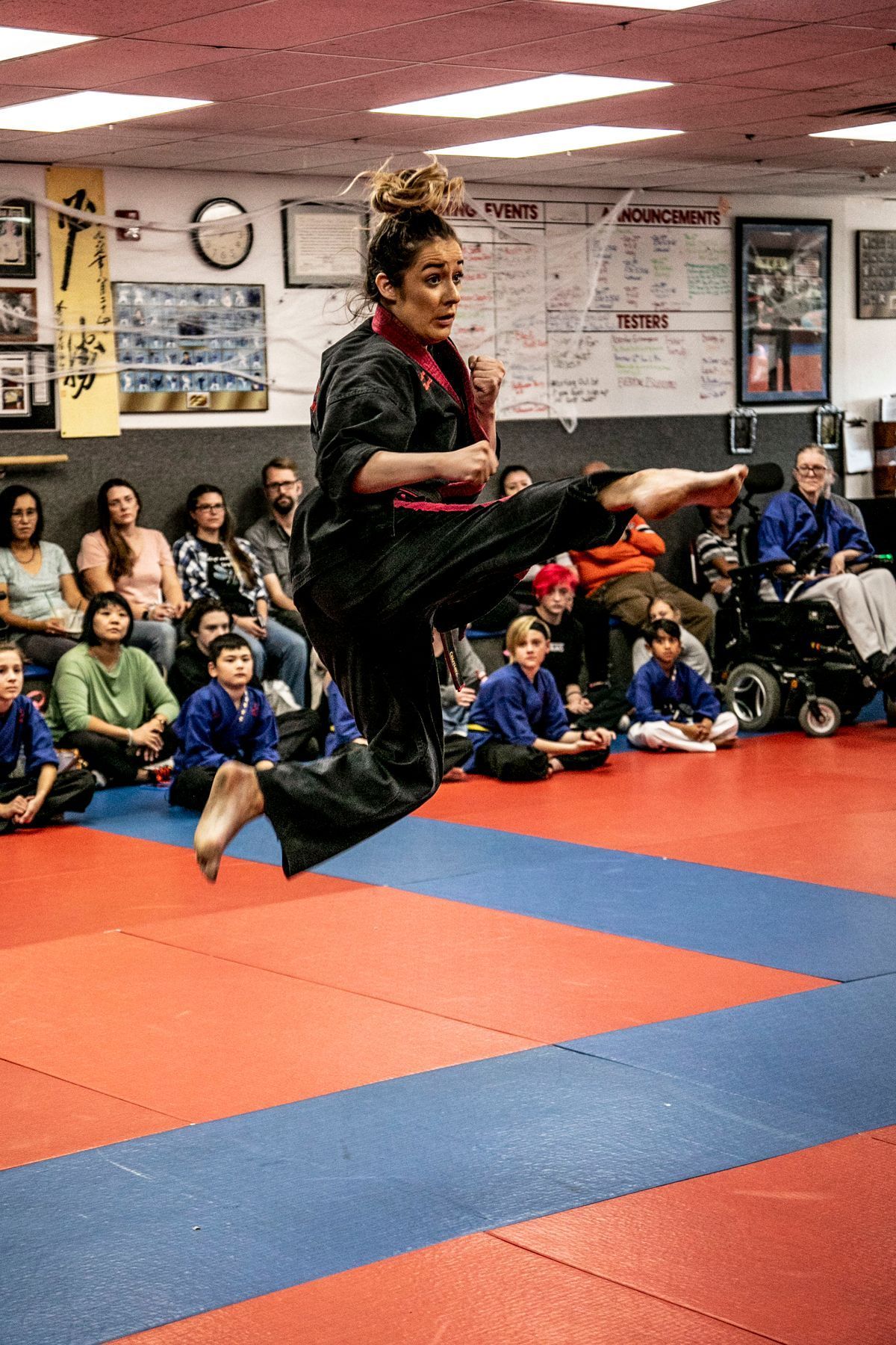 A woman is jumping in the air while practicing karate in a gym.