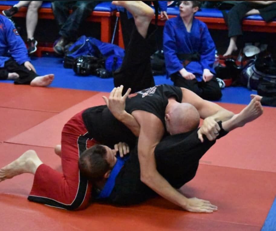 Two men are wrestling on a mat with a crowd watching