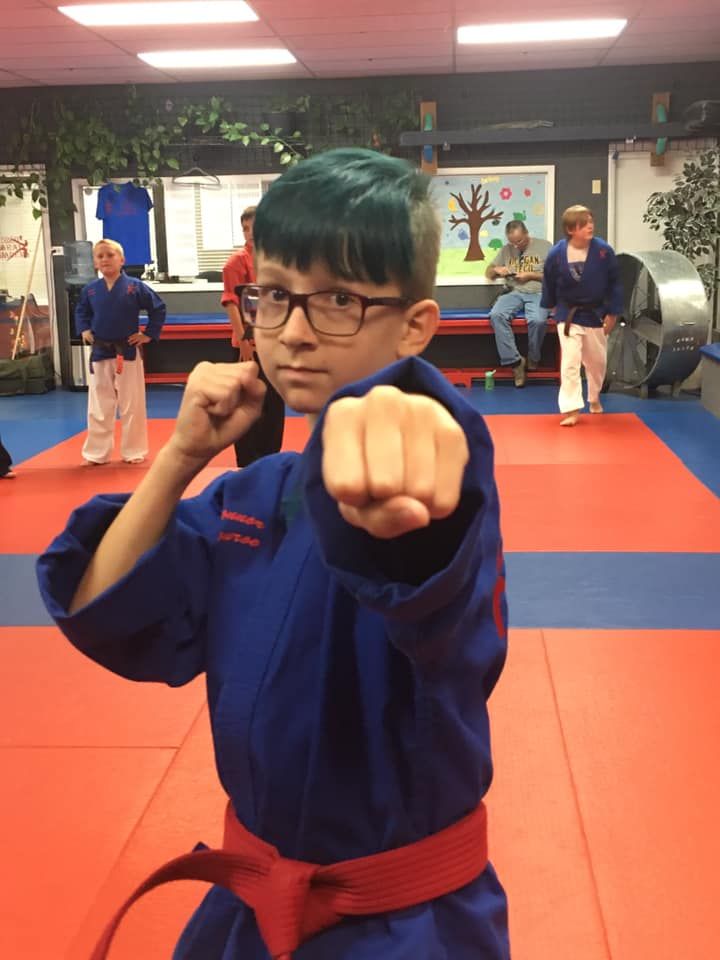 A young boy wearing a blue karate uniform and a red belt