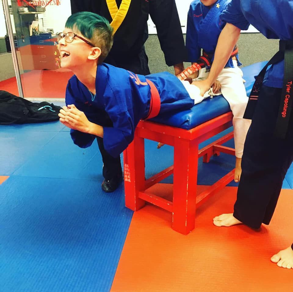 A boy in a blue karate uniform is laying on a red bench