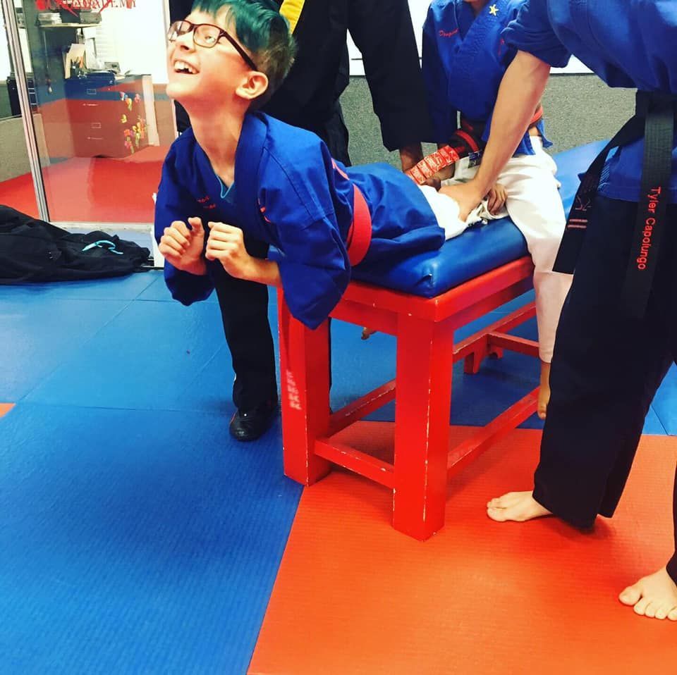 A boy in a blue uniform is laying on a red stool