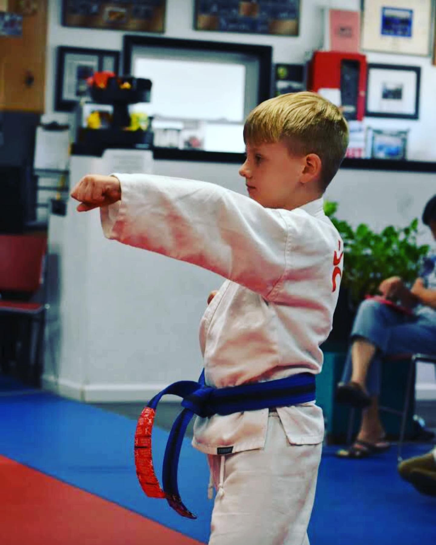 A young boy is wearing a white karate uniform and a blue belt.