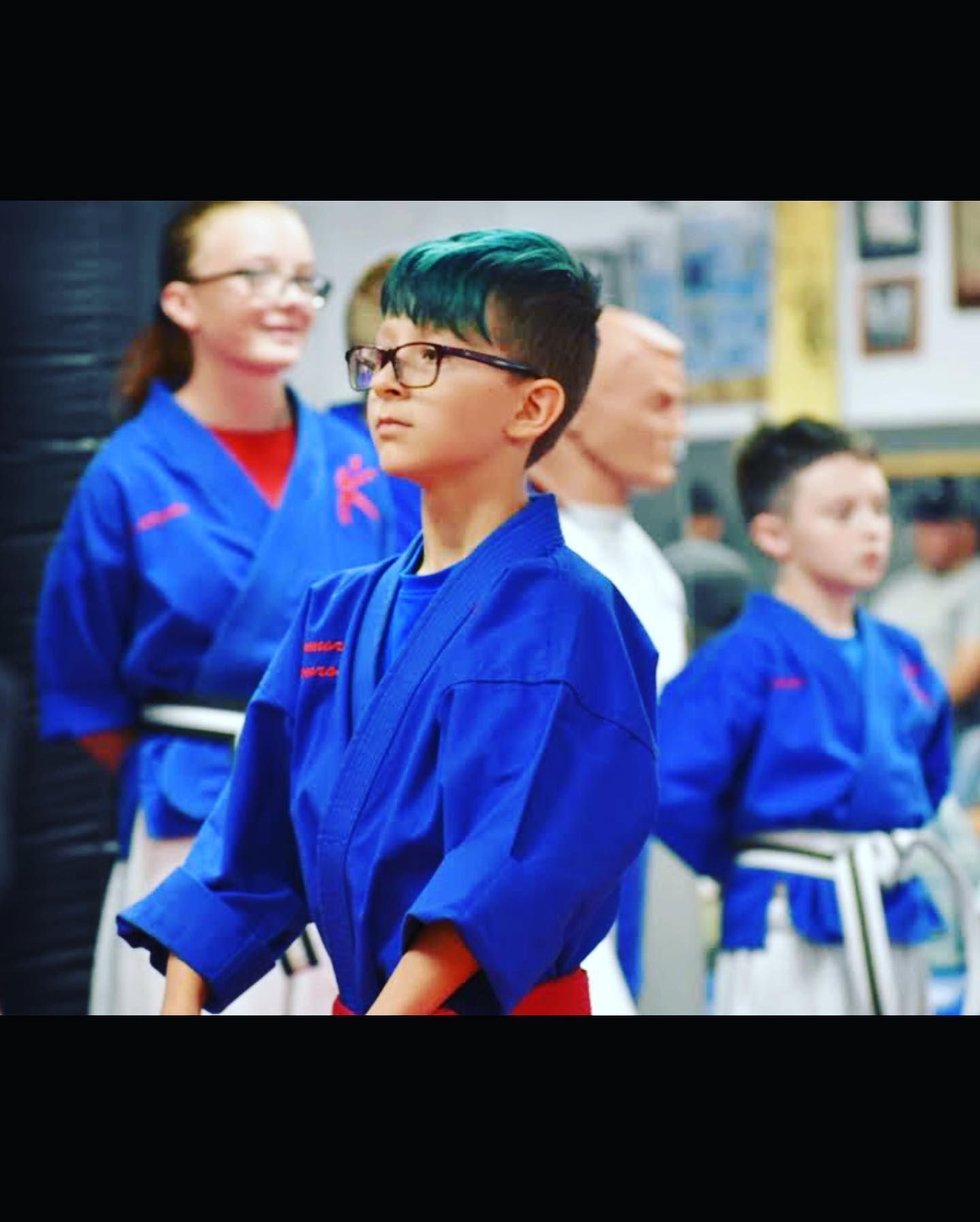 A boy with green hair and glasses is wearing a blue karate uniform.