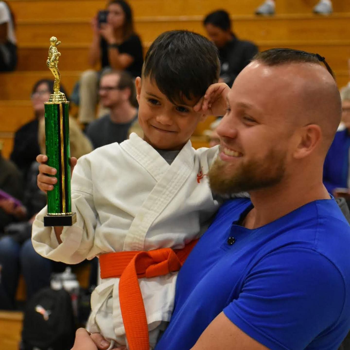 A man is holding a young boy who is holding a trophy