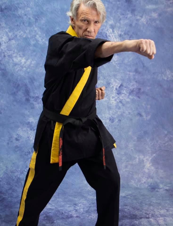 A man in a black and yellow karate uniform is standing in front of a blue background