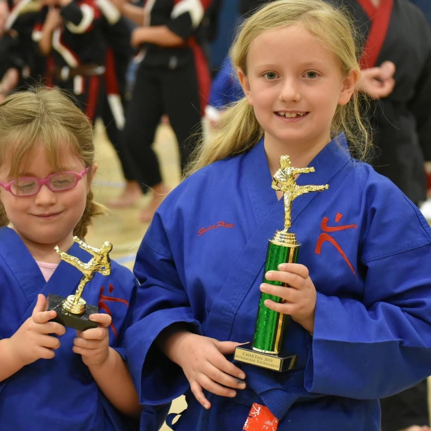 Two young girls in blue karate uniforms holding trophies