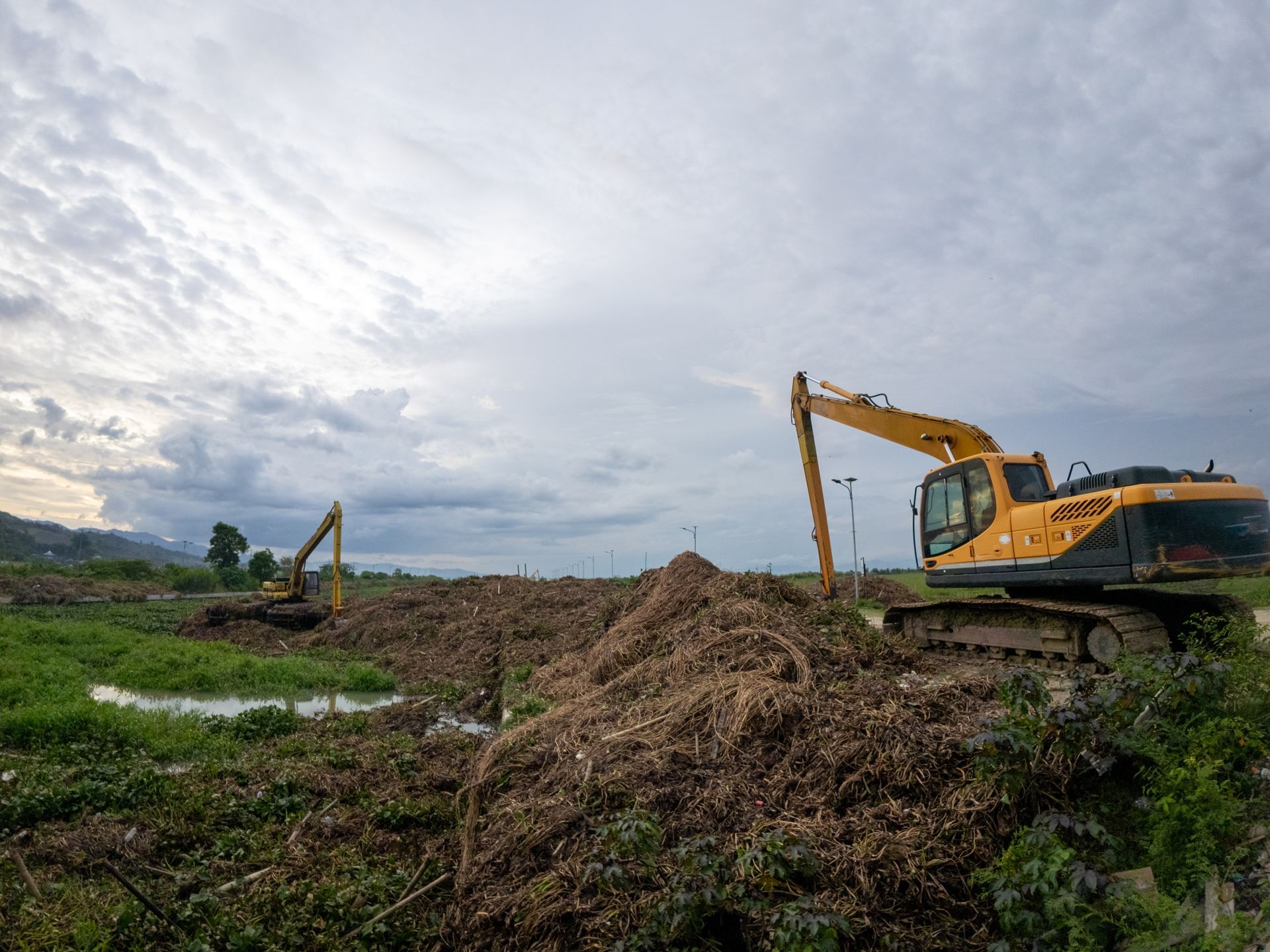 Two yellow excavators on a field of debris under a cloudy sky.