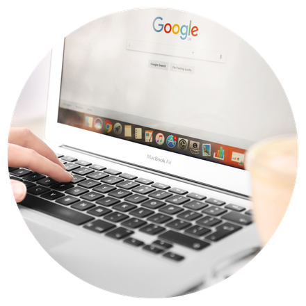 A person is typing on a laptop with a google search bar on the screen.