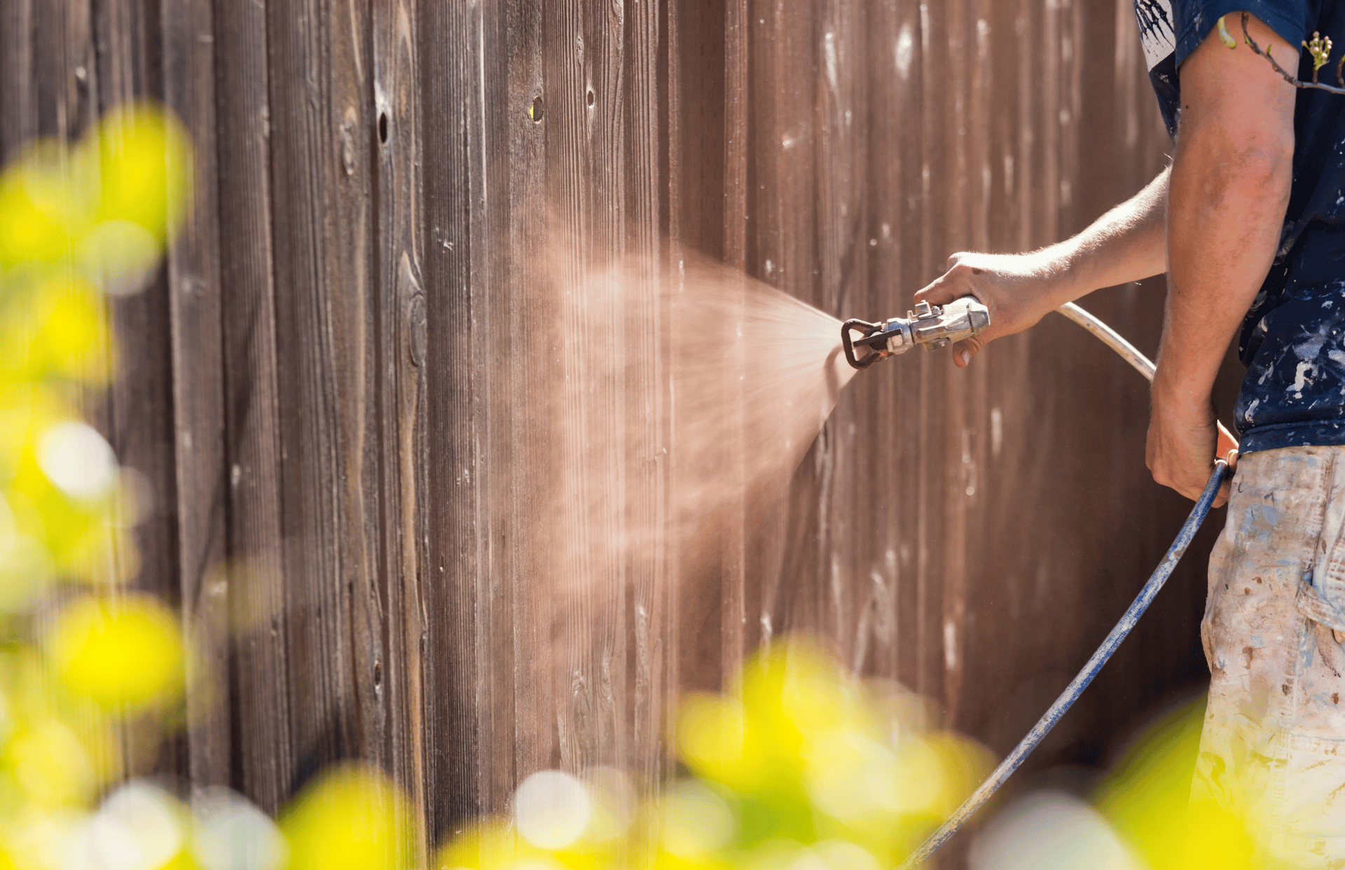 A man is spraying paint on a wooden fence with a hose.