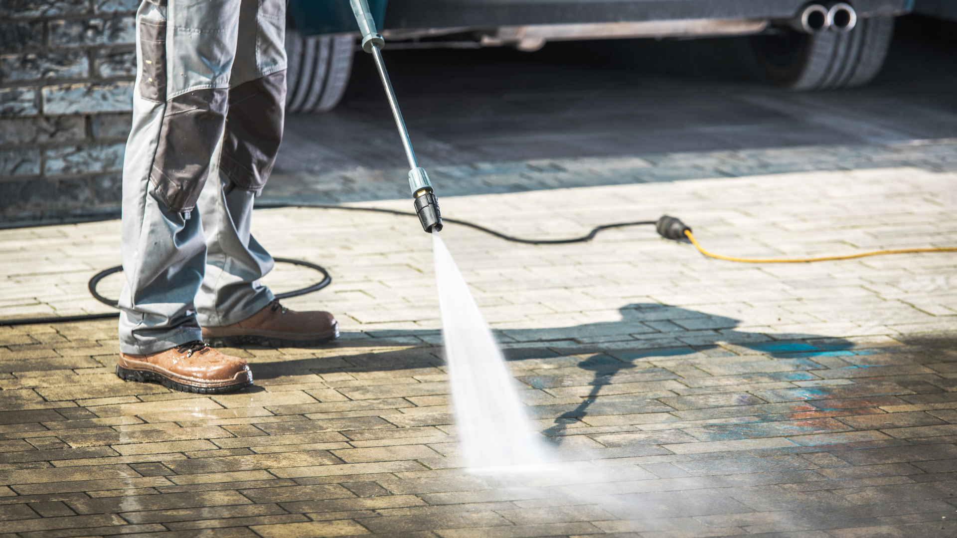 A man is using a high pressure washer to clean a brick driveway.