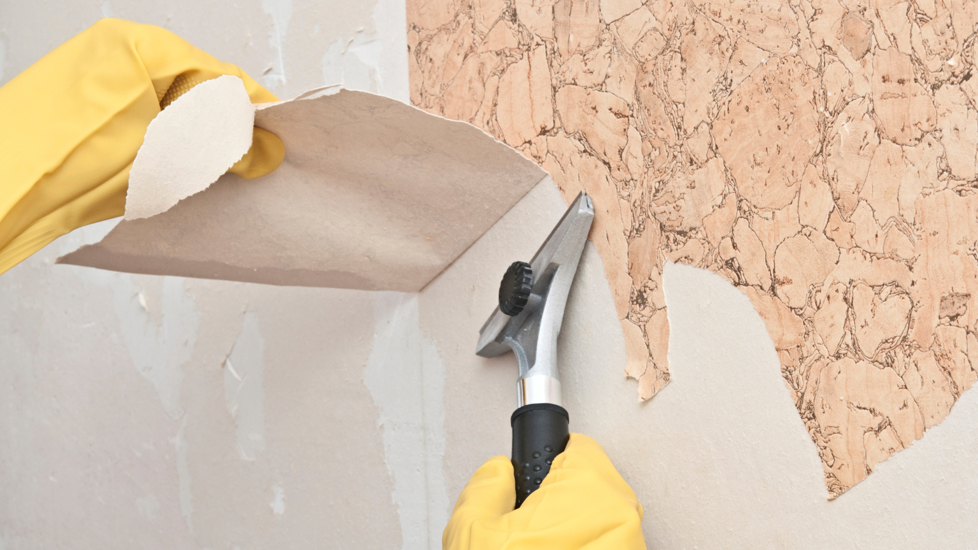 A person is removing wallpaper from a wall with a spatula.