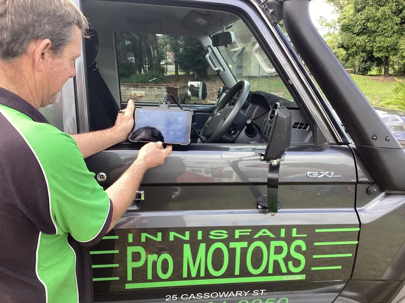 Man holding a tablet, looking into a car. 