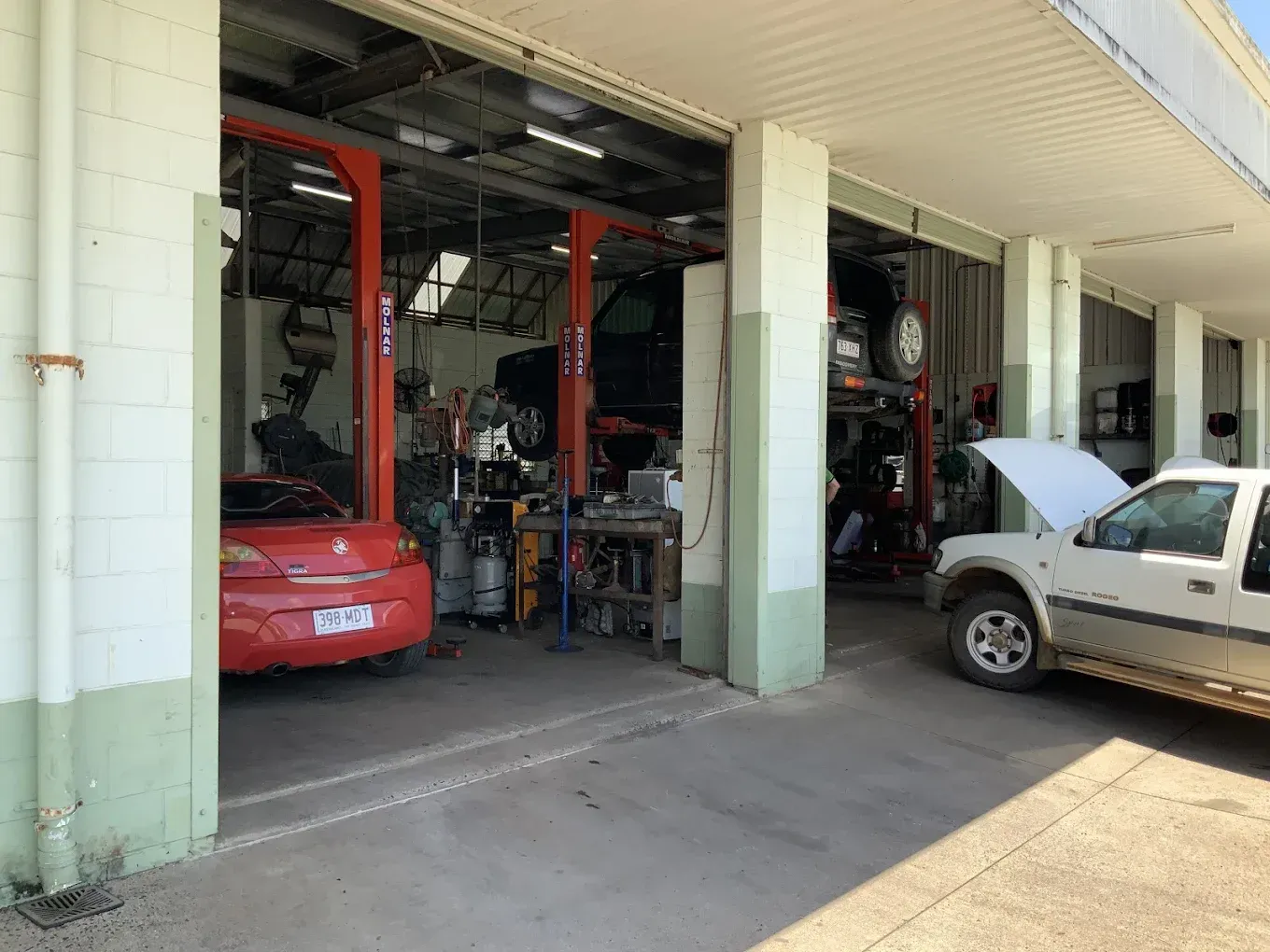 Car repair shop with three vehicles: a red car, a car on a lift, and a white pickup truck — Innisfail Pro Motors in Innisfail, QLD
