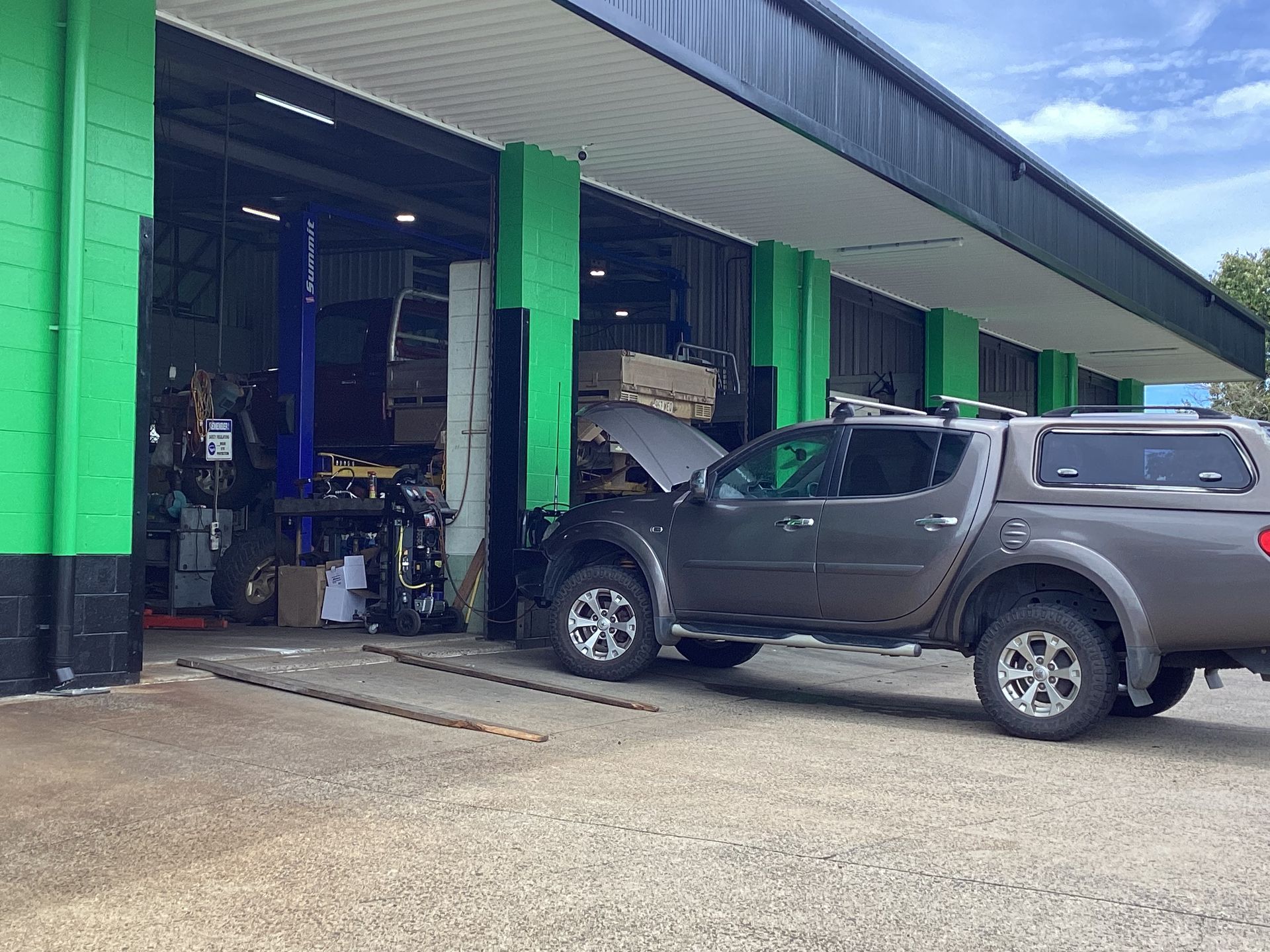 Gray truck with open hood at a garage bay. Green and black building, open garage doors — Innisfail Pro Motors in Innisfail, QLD