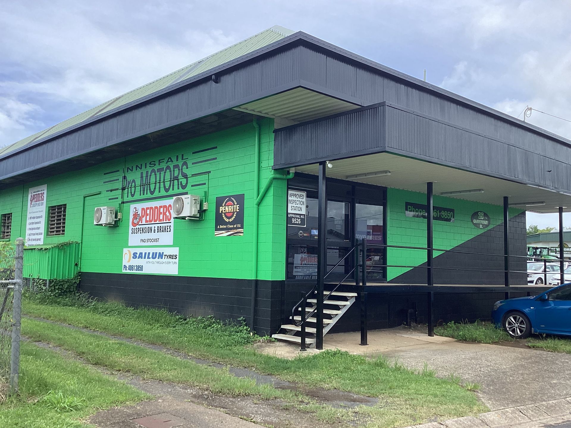 Green and black commercial building: "AD" store, entrance with steps, overcast sky — Innisfail Pro Motors in Innisfail, QLD