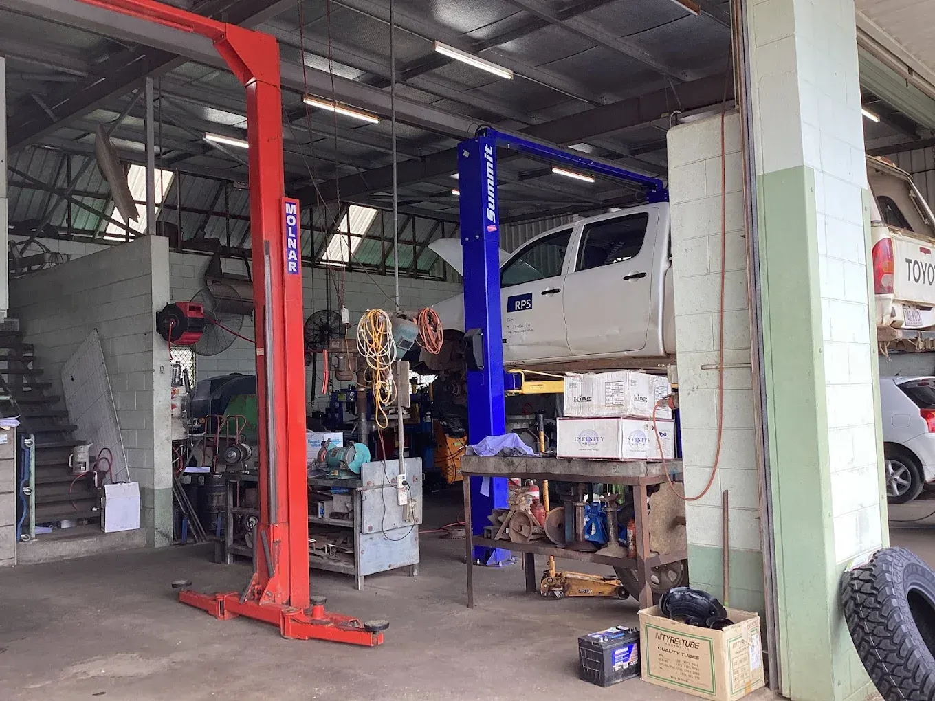 An auto repair shop with a white truck on a lift. Tools and equipment are scattered about.