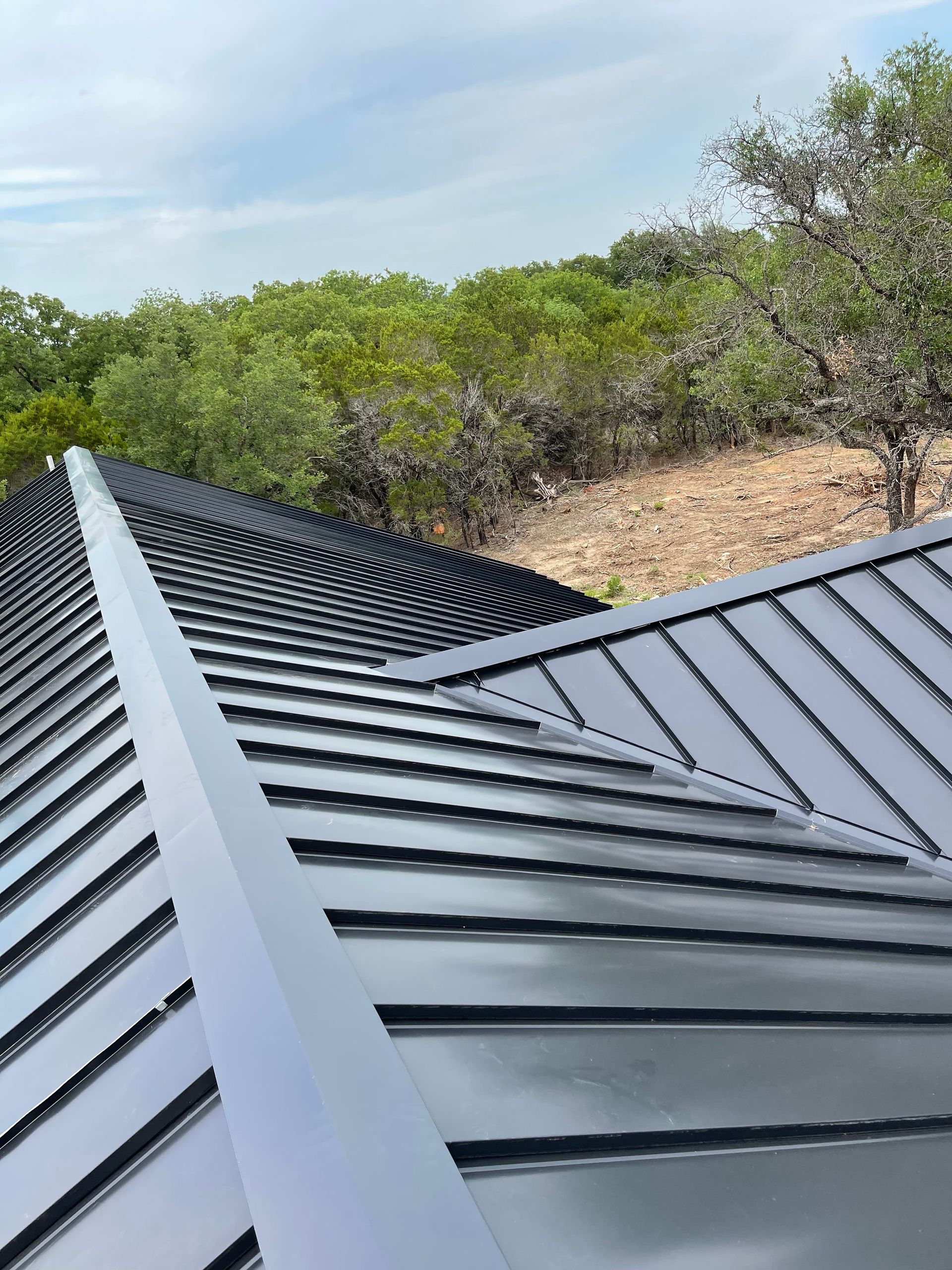 A close up of a black metal roof with trees in the background.