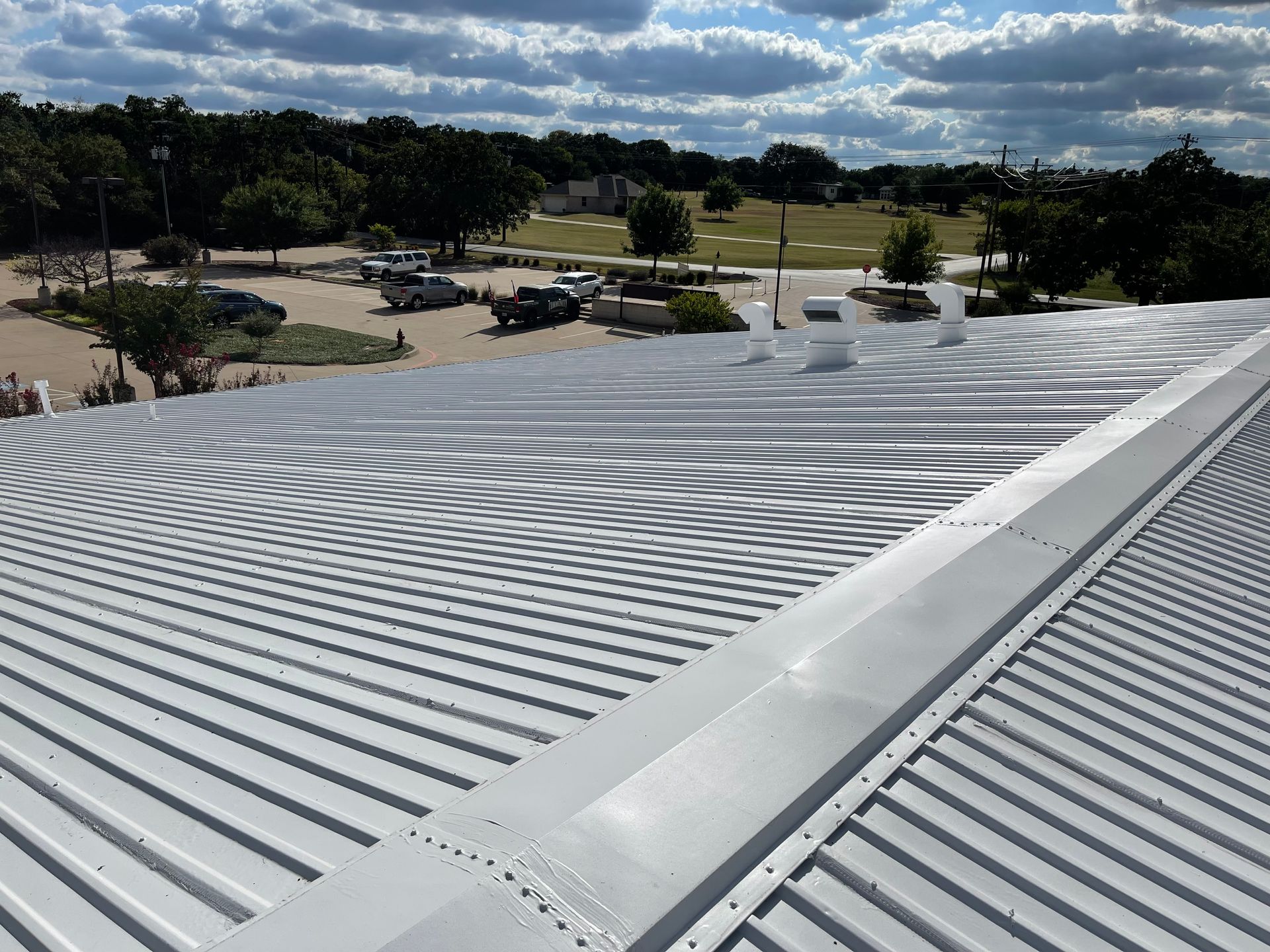 The roof of a building with a parking lot in the background.