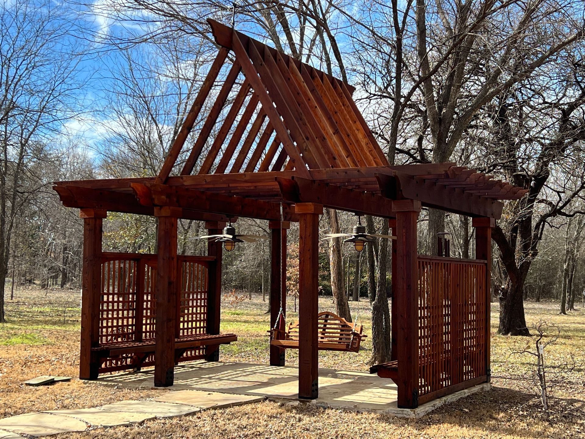 A wooden gazebo with a swing in the middle of a park.