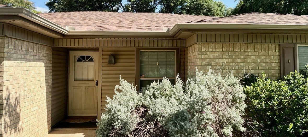 The front of a brick house with a brown roof and a white door.