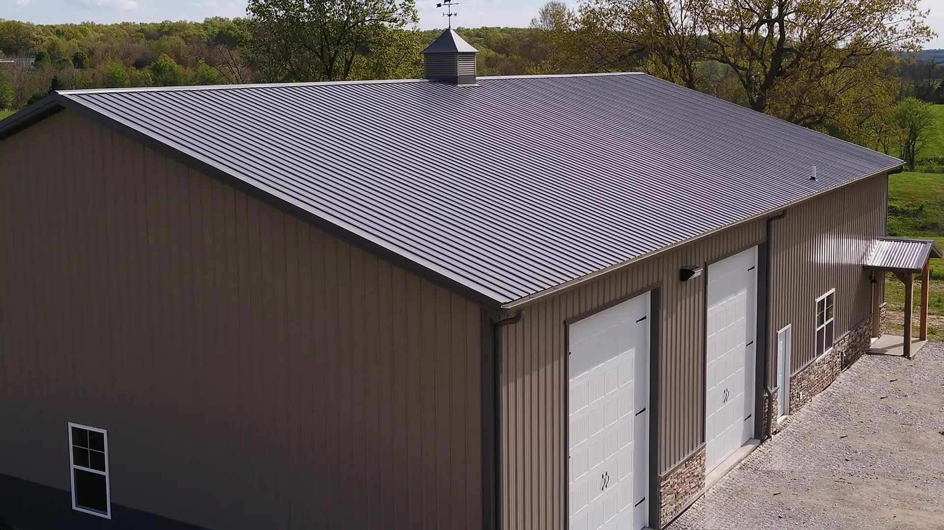 Dark gray metal tile roof with chimney and wood trim against a cloudy sky.