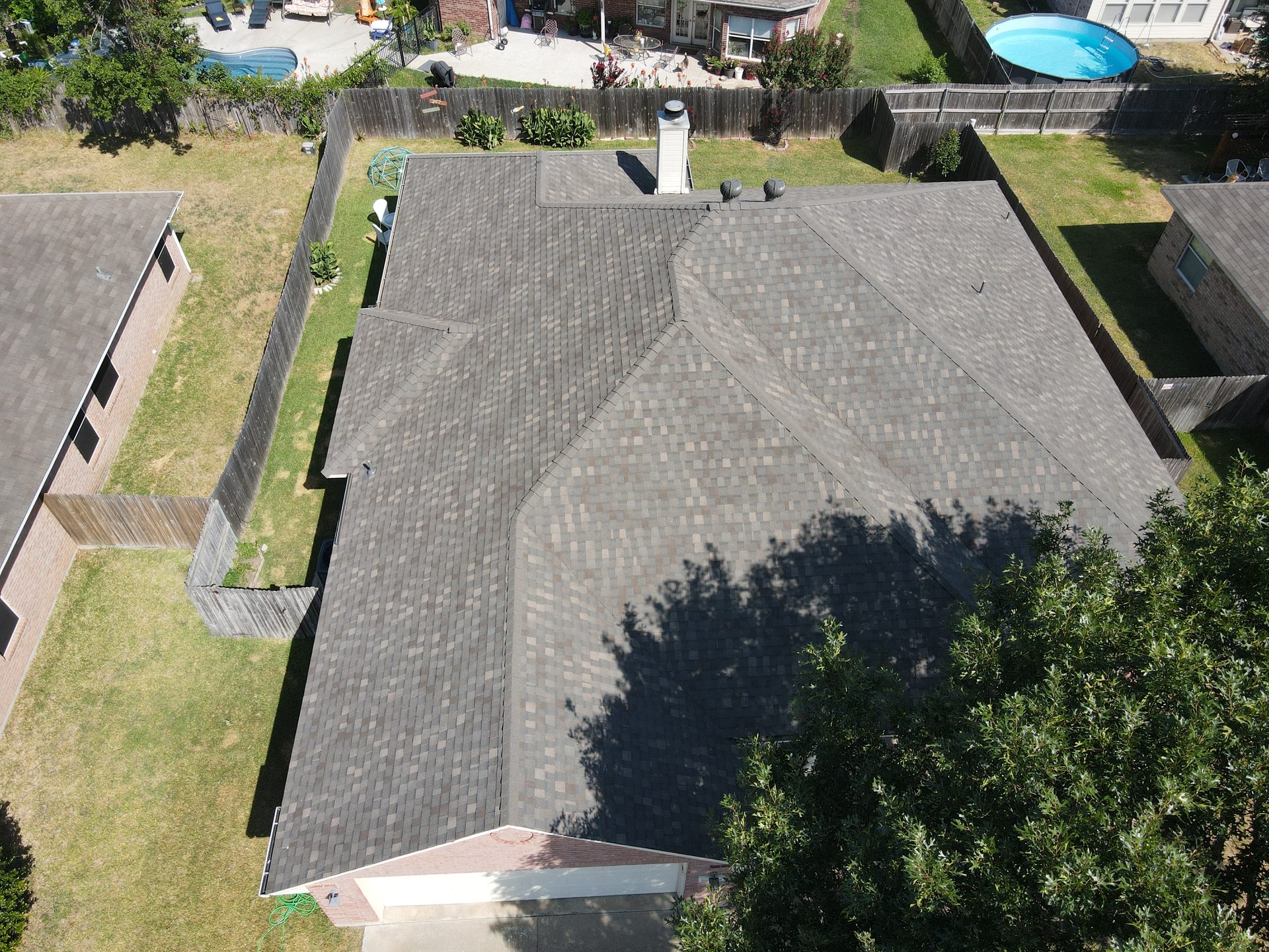An aerial view of a house with a roof and a pool in the backyard.