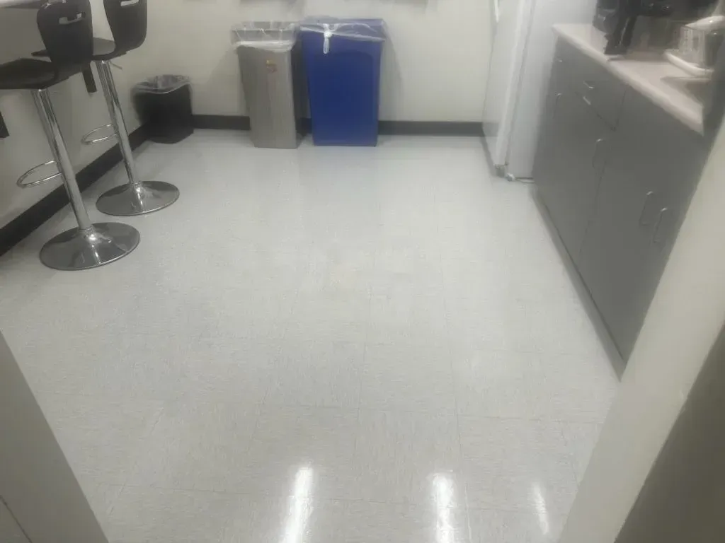 A shiny white floor in a room, with a tall stool, trash cans, and a blue bin against the wall.