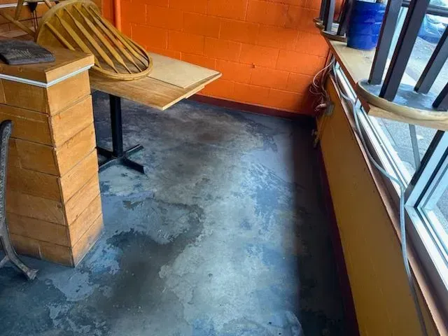 Wet concrete floor in a restaurant corner, with an orange wall, a table, and a window.