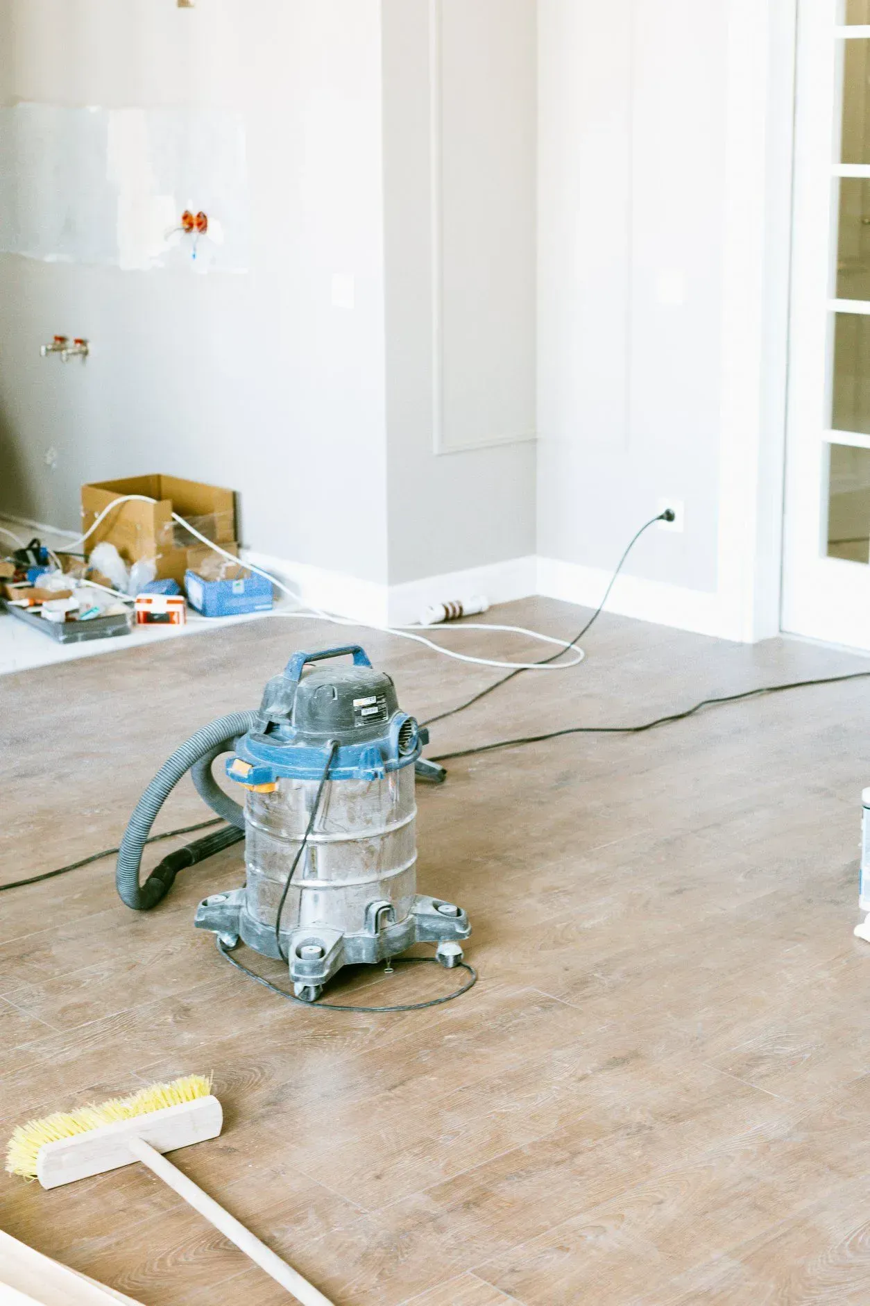 Construction site: Blue and silver vacuum cleaner on wooden floor, broom nearby.