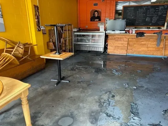 Interior of a cafe with water damage on the floor, tipped chairs, and empty tables.