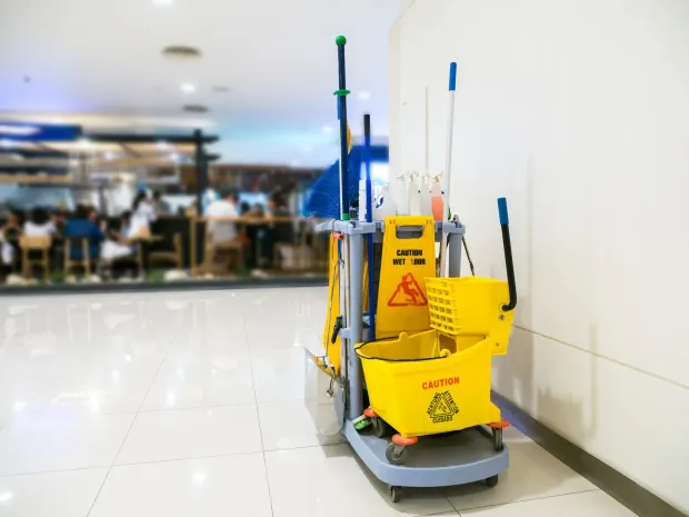 Yellow cleaning cart with buckets and caution sign on a shiny floor in a public space.