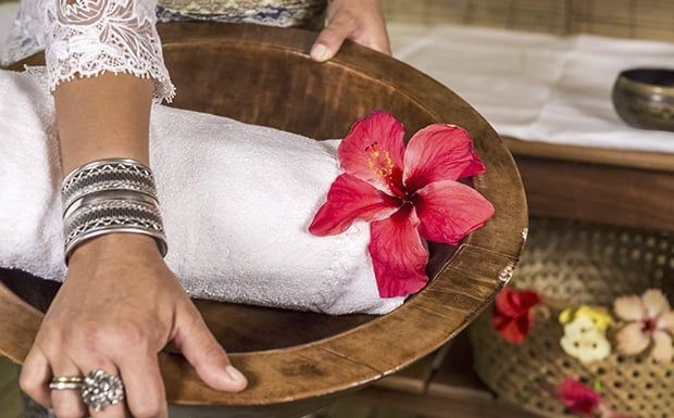 Uma mulher está sentada em uma tigela de madeira com uma flor dentro.