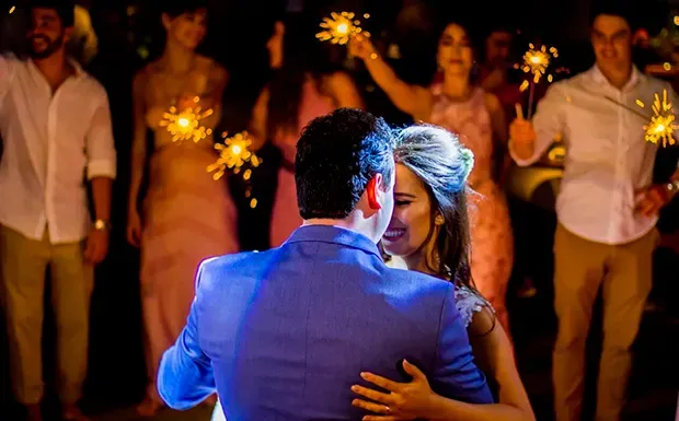 Uma noiva e um noivo estão dançando na recepção do casamento enquanto seguram estrelinhas.